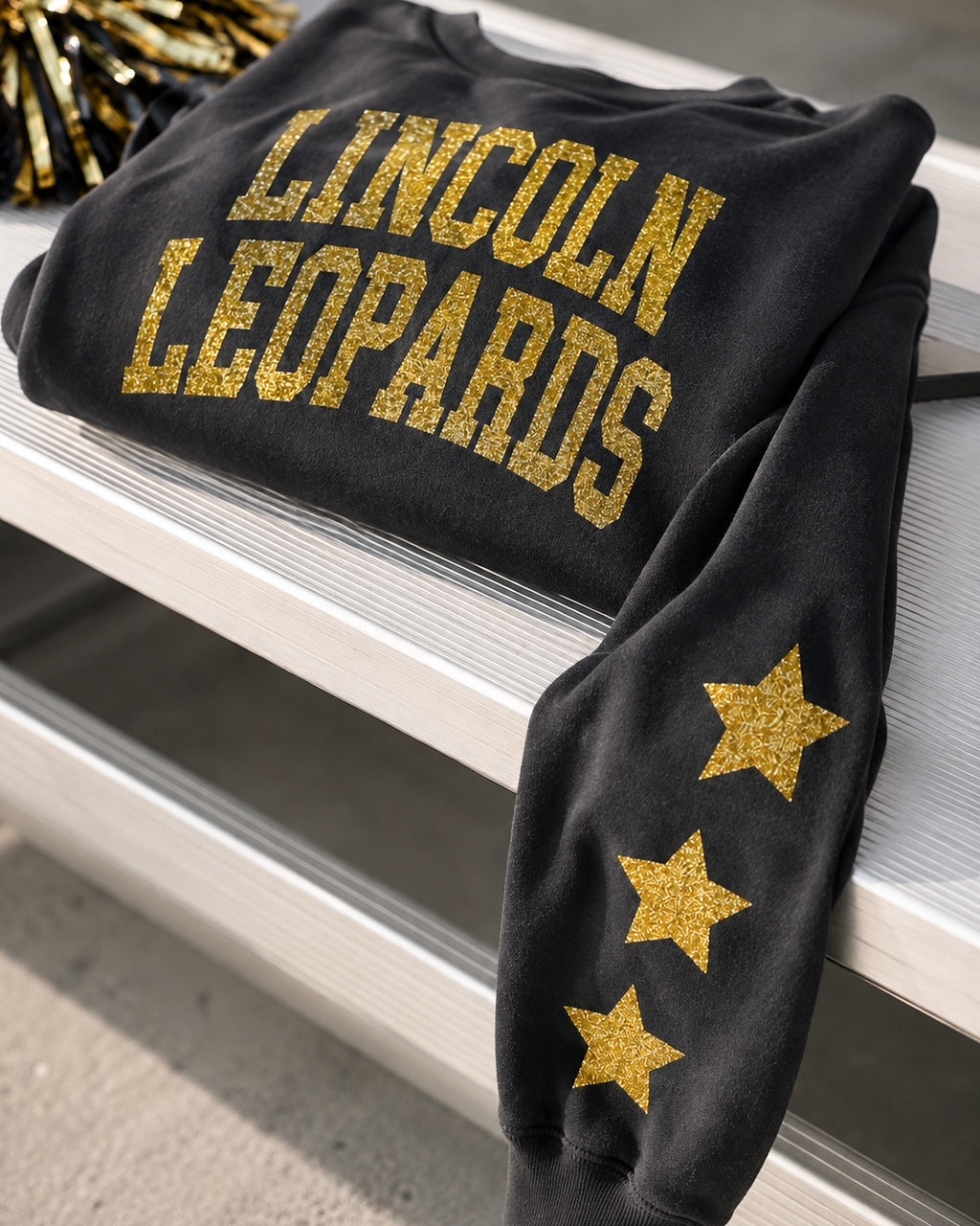 Black All-Star Leopard Sweatshirt displayed on school bleachers with gold-glitter lettering and sleeve stars