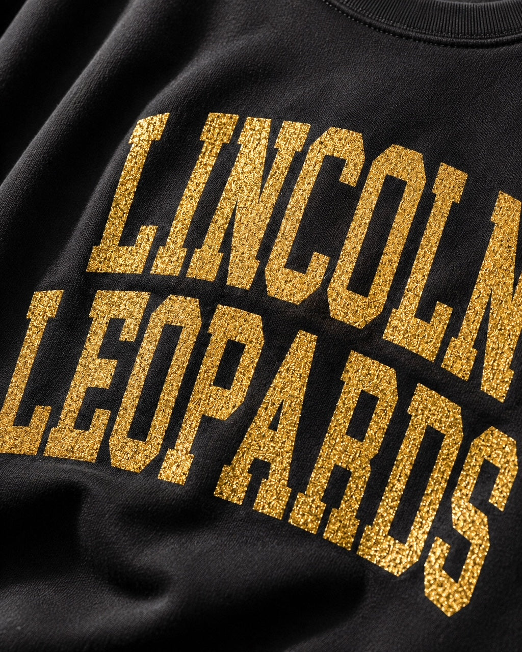 Close-up of gold-glitter Lincoln Leopards lettering on the black All-Star Leopard Sweatshirt