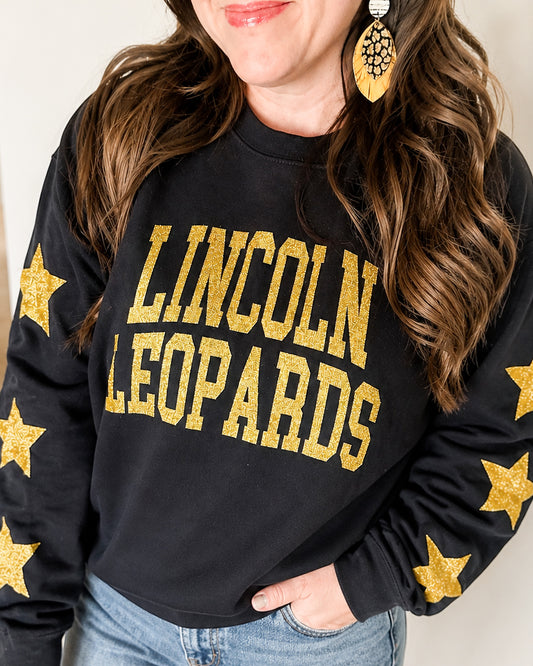 Woman wearing the black All-Star Leopard Sweatshirt with gold-glitter Lincoln Leopards lettering and stars down both sleeves