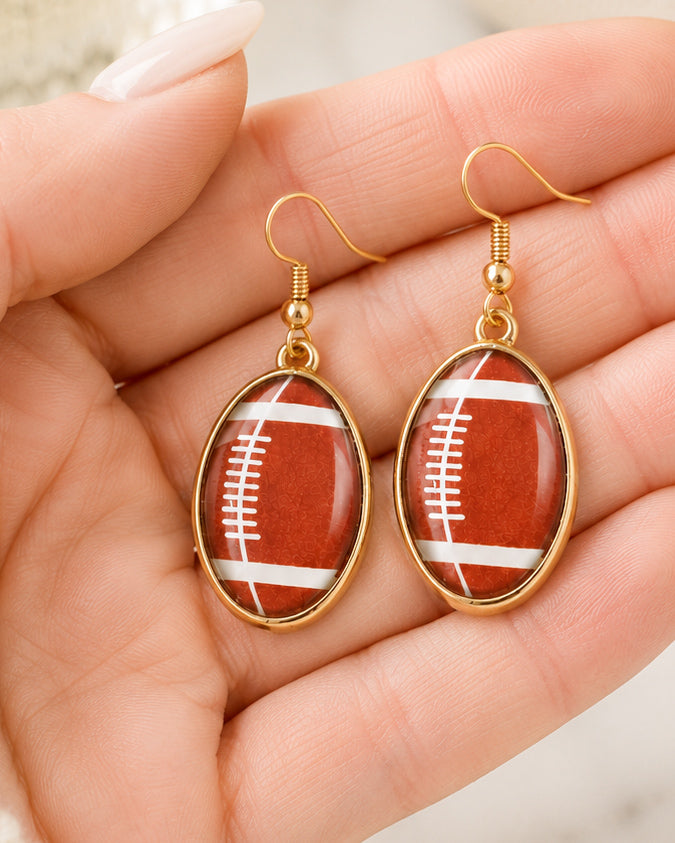 Gold football earrings shown in hand for size reference.