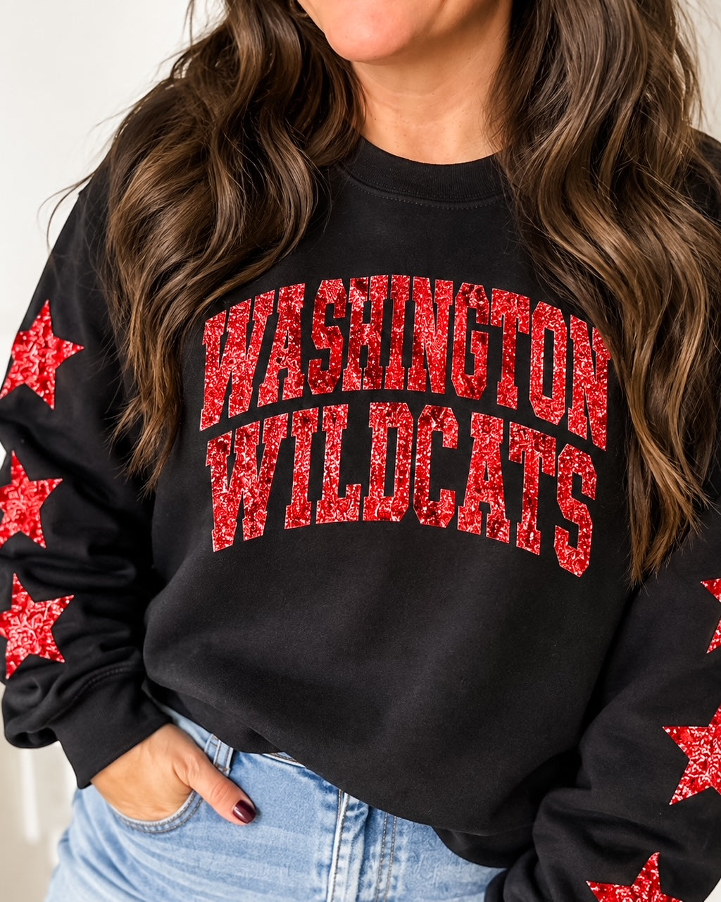 Woman modeling the black All-Star Wildcat Sweatshirt with arched red glitter Washington Wildcats lettering and coordinating sleeve stars.