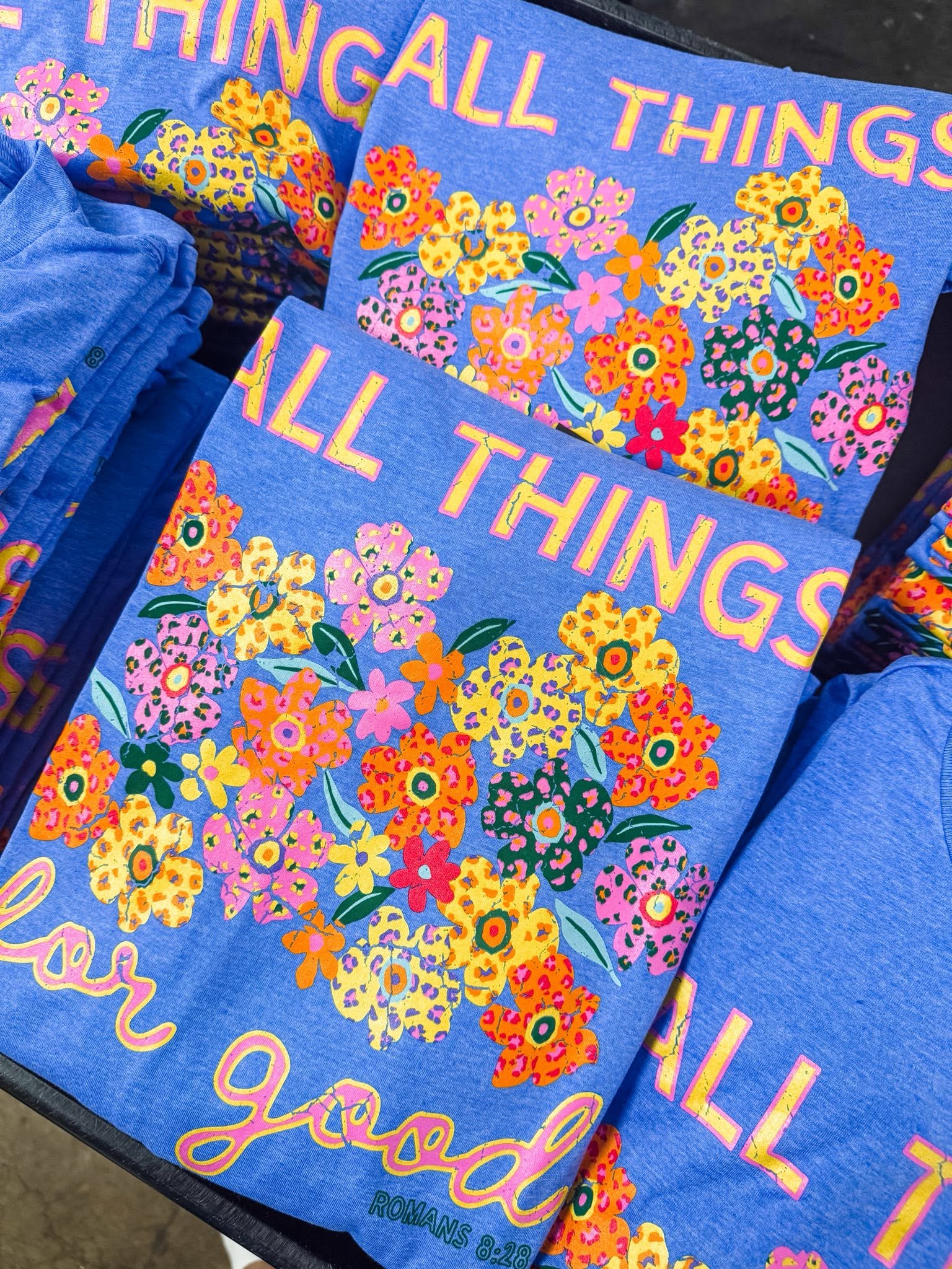 Stack of colorful All Things for Good Romans 8:28 graphic tees