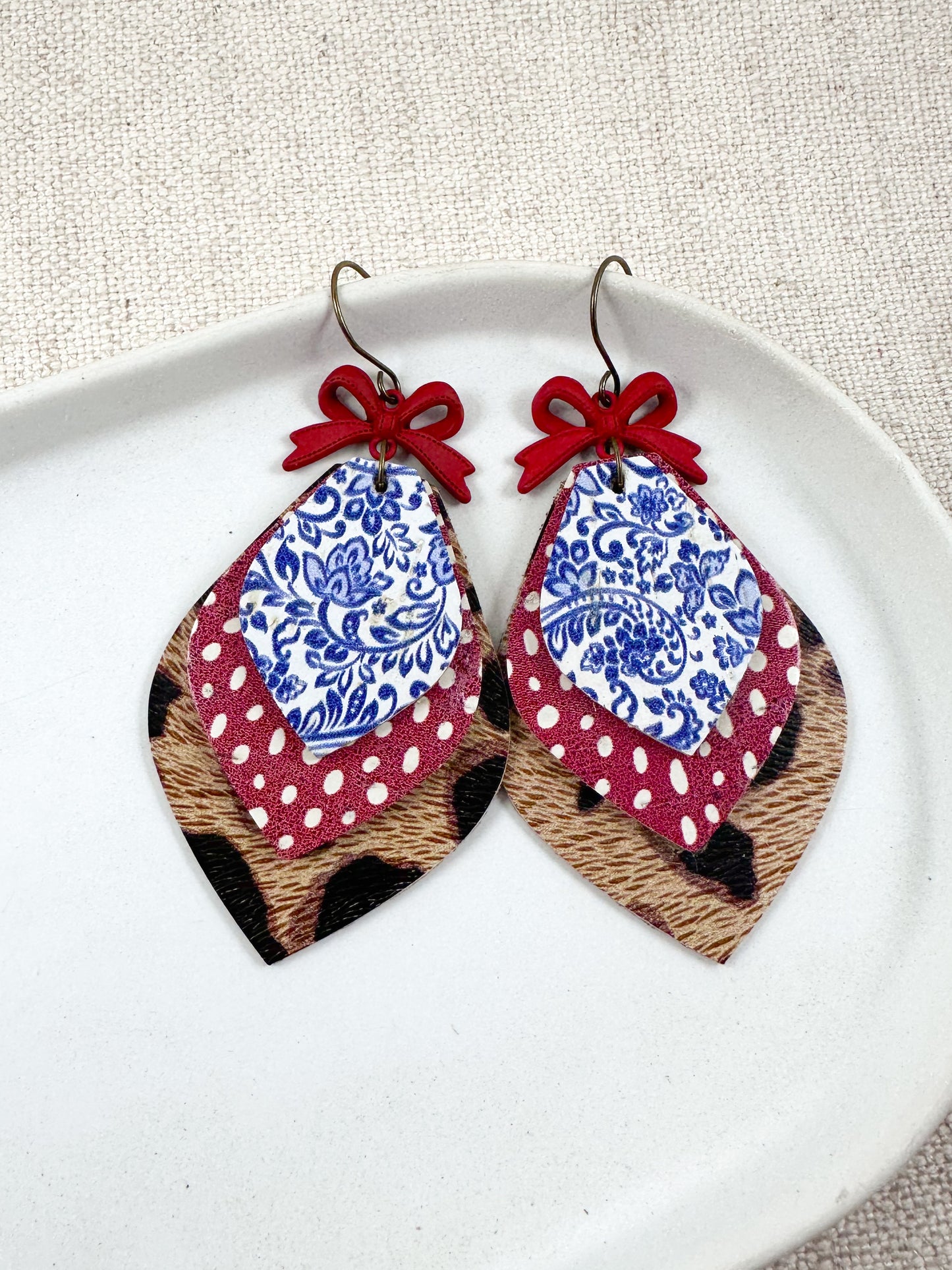Flat lay of American Honey Earrings featuring layered cork and genuine leather with red bows, blue and white floral print, red polka dots, and leopard print details.
