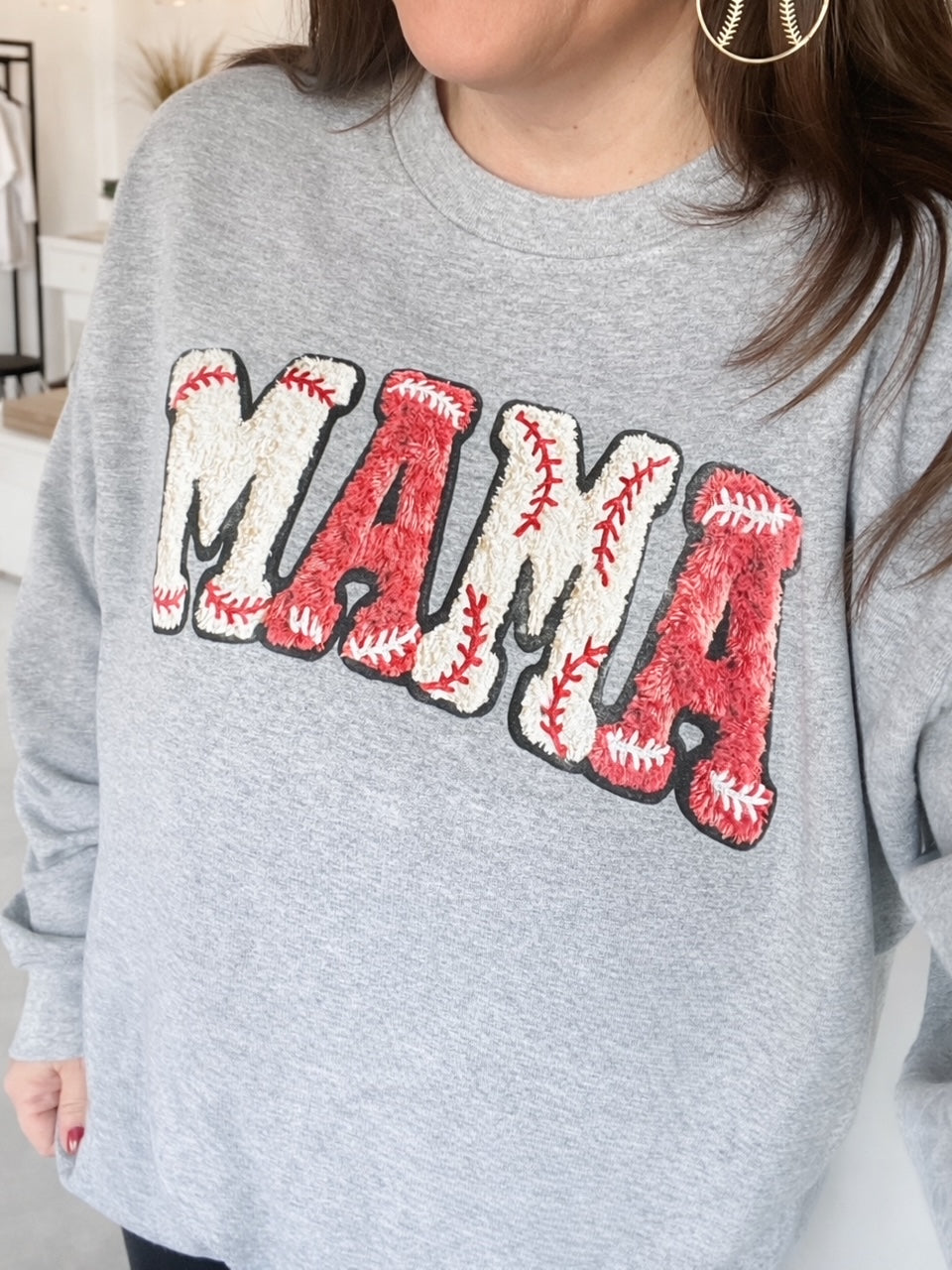 Woman wearing heather gray shirt with large red MAMA graphic with baseball stitch detailing.