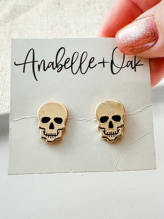 Close-up of gold skull studs showing polished finish and fine details.