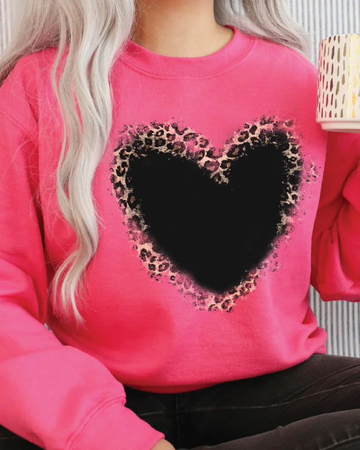 Close-up of a bright pink sweatshirt with a blackwashed leopard heart graphic, styled with dark jeans and a patterned coffee mug in hand