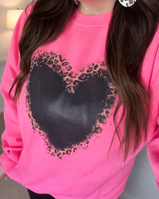 Model wearing a bright pink sweatshirt with a blackwashed leopard heart graphic on the front