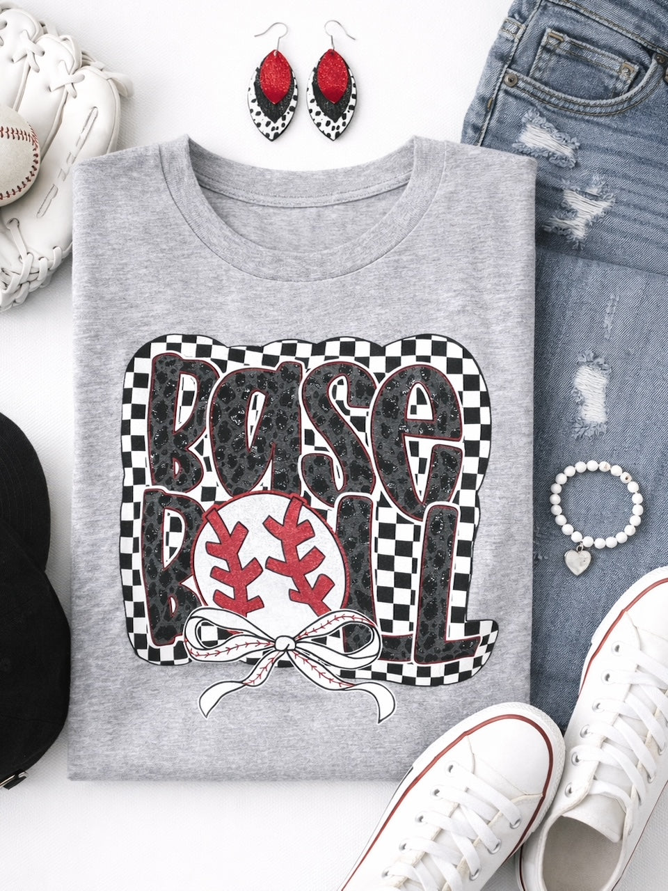 Heather gray baseball graphic shirt folded in flatlay with red leather earrings, distressed jeans, white sneakers, and baseball accessories.