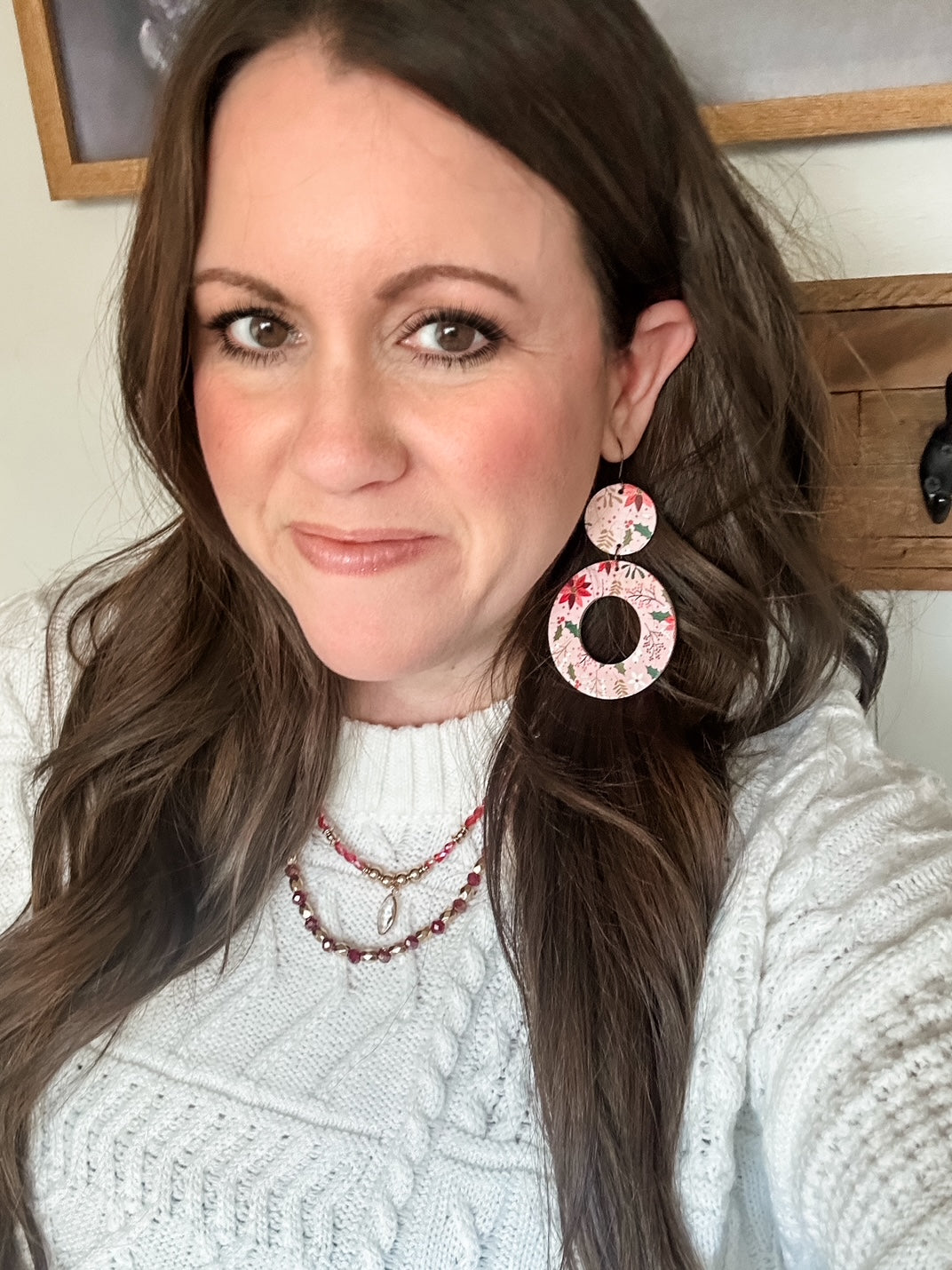 Model wearing Blush Poinsettia Cork circular earrings with a white cable knit sweater and layered red and gold beaded necklaces.