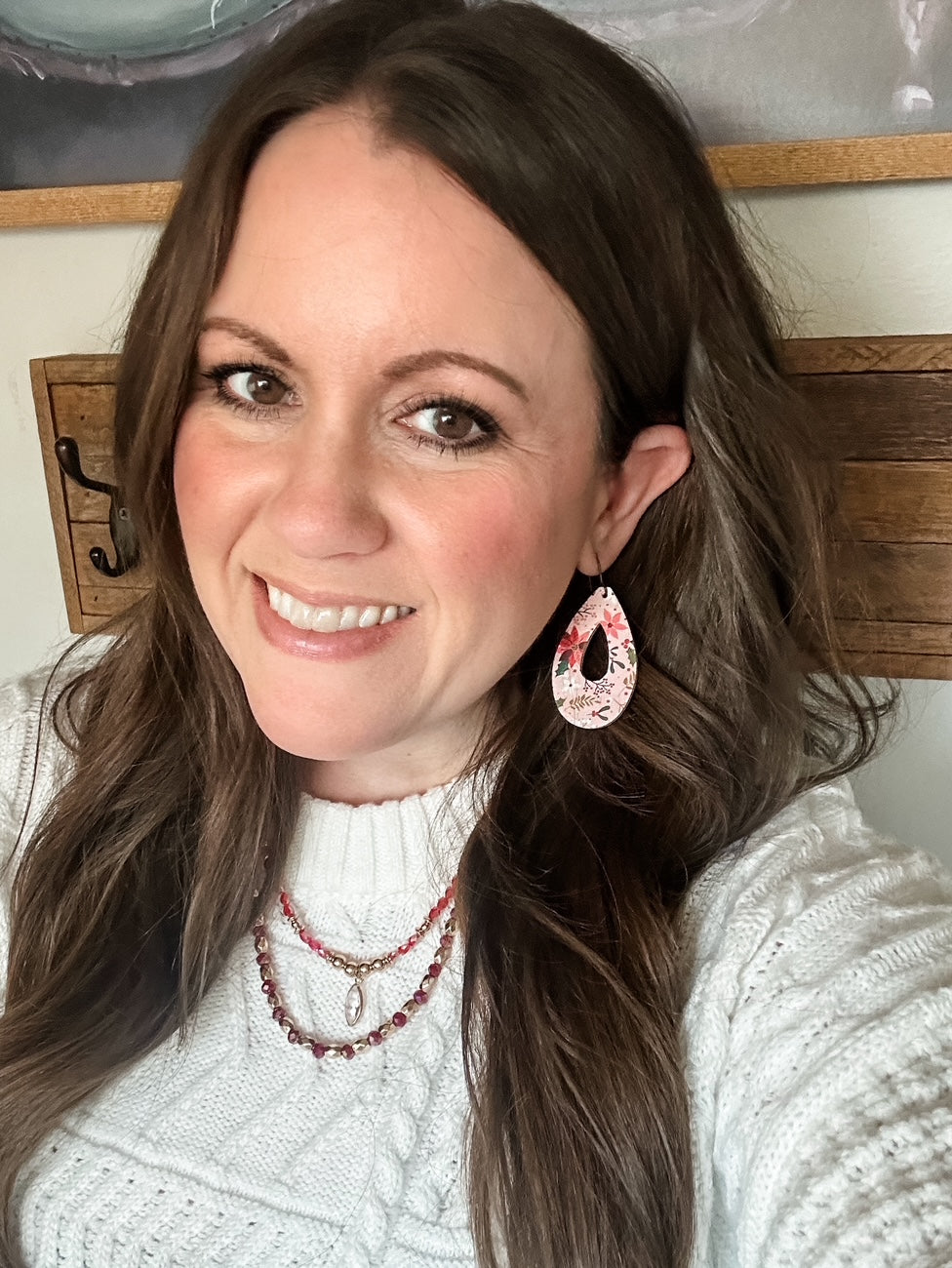 Model wearing Blush Poinsettia Cork teardrop cutout earrings with a white cable knit sweater and layered red and gold beaded necklaces.