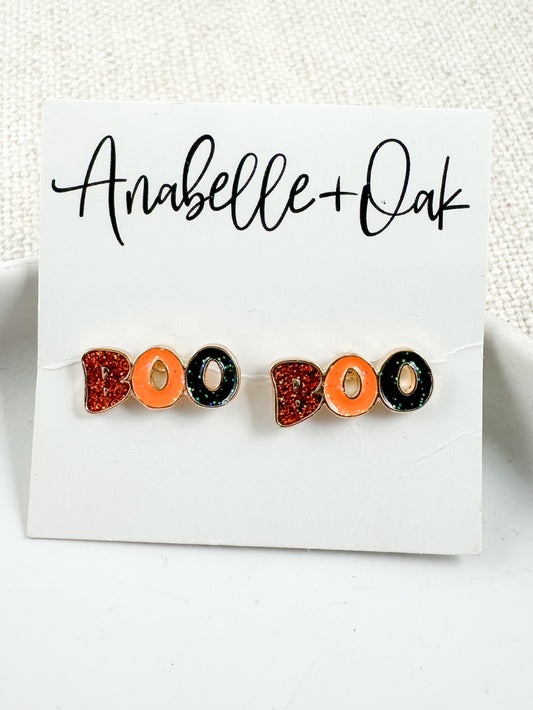 Close-up of Boo Crew Stud earrings with orange, black, and red glitter enamel on white Anabelle+Oak card