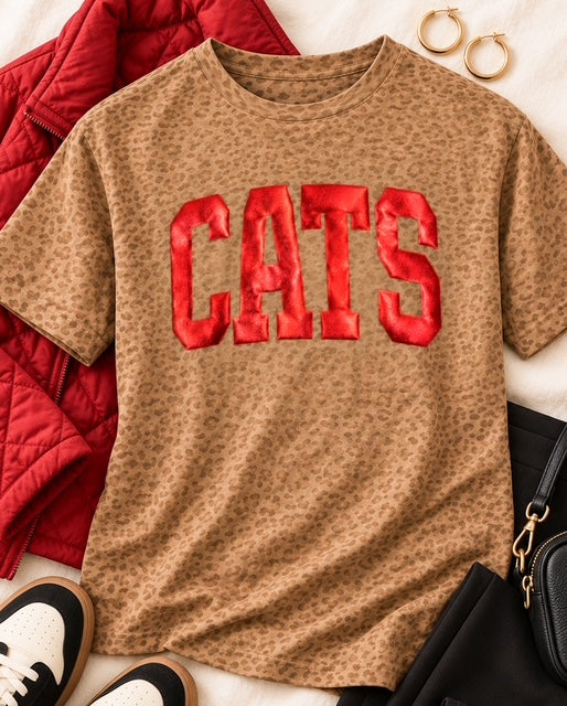 Cats in the Wild Tee styled with a red quilted jacket, black pants, retro sneakers, and a black crossbody bag.