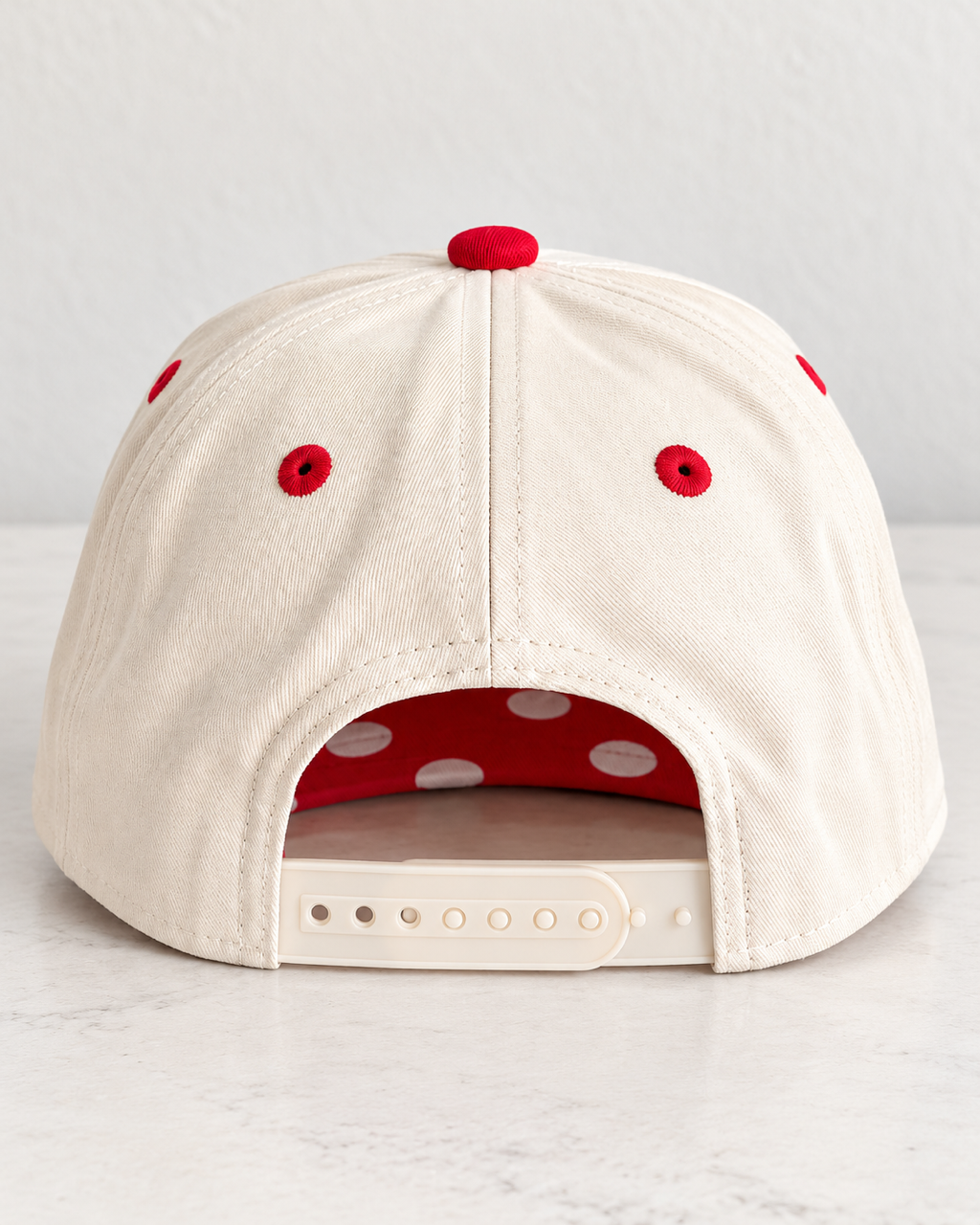 Back view of cream CATS Pep Rally Hat showing red eyelets, adjustable snap closure, and polka-dot bill.