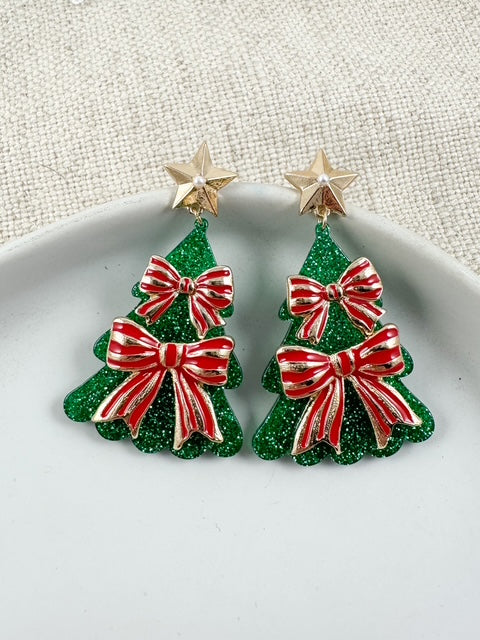 Glittered green Christmas tree earrings with red bows and gold star tops on a white plate