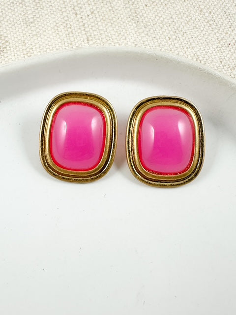 Hot pink rectangular stud earrings with gold frames on a white plate