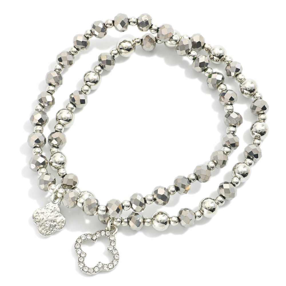 Two silver beaded stretch bracelets with faceted beads and clover charms on a white surface.