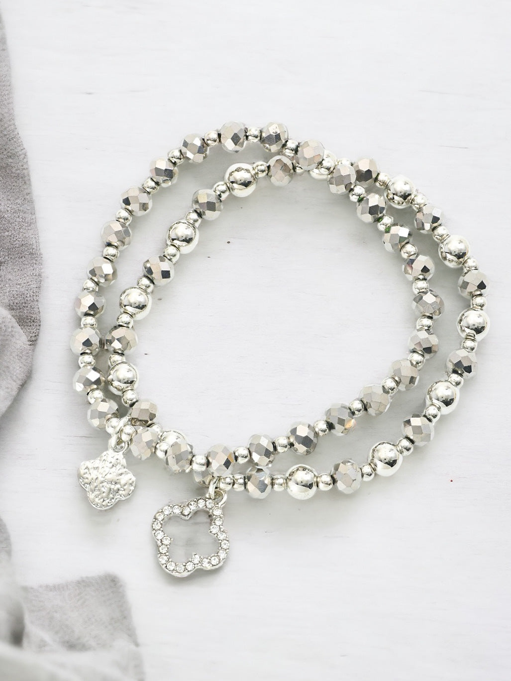 Two silver stacking bracelets with round and faceted beads and crystal clover charm on a light background.