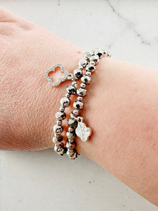 Silver beaded stretch bracelet set worn on a wrist, featuring faceted beads and a clover charm.