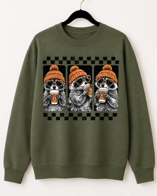 Green Gildan Cozy Little Bandits crewneck sweatshirt with three raccoons in orange beanies holding coffee.