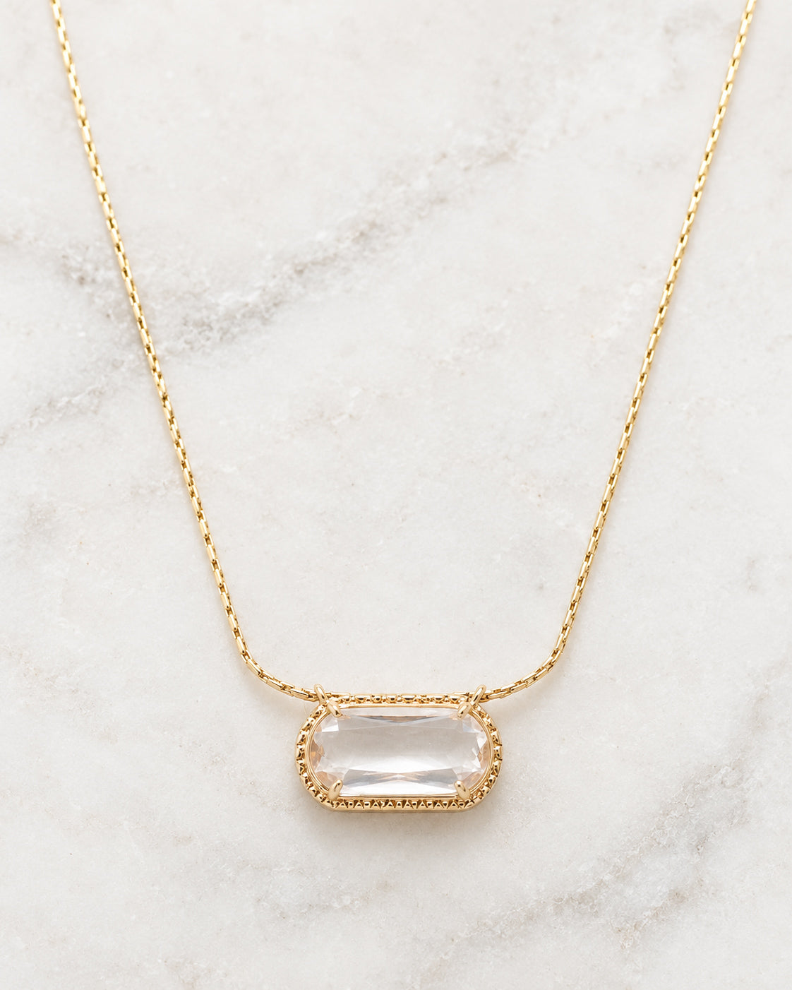 Detailed view of the Crystal Clear Necklace featuring a sparkling clear faceted bead in an ornate gold-tone setting with a delicate chain on white marble.