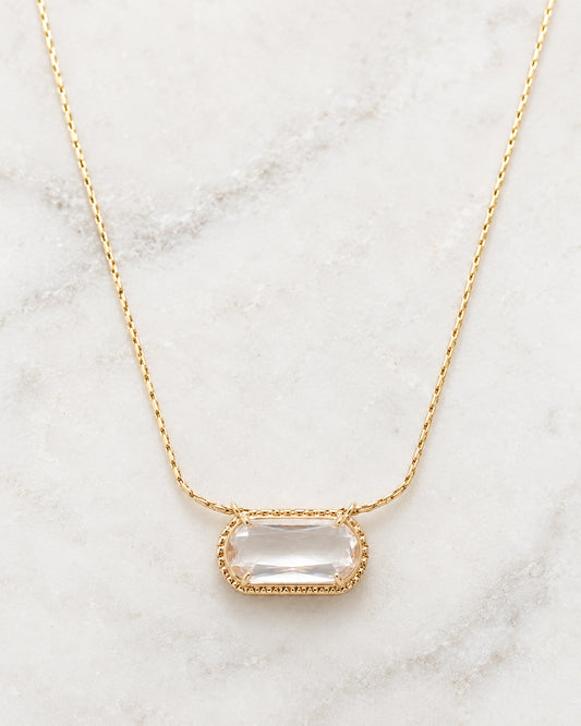 Detailed view of the Crystal Clear Necklace featuring a sparkling clear faceted bead in an ornate gold-tone setting with a delicate chain on white marble.