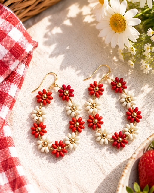 Red floral statement earrings styled with strawberries and a red gingham cloth.