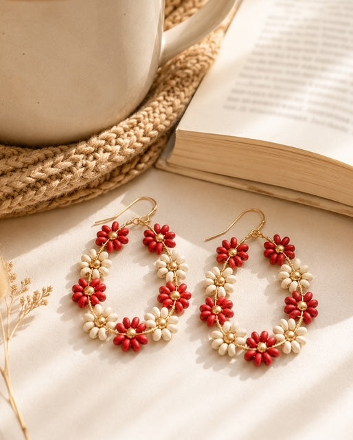 Red and ivory floral earrings styled beside a coffee mug and open book.