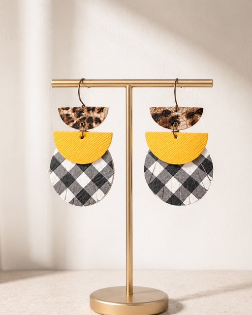 Dress Code Earrings hanging from a gold jewelry stand against a creamy white background.