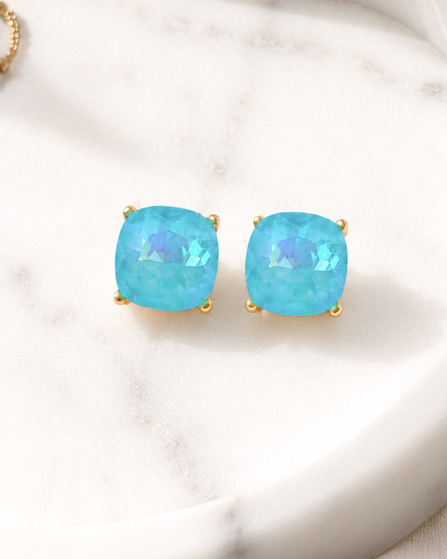 Turquoise iridescent stud earrings styled in a white marble dish with gold-tone hardware.