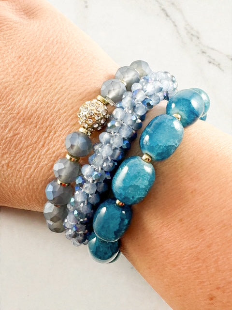 Three blue beaded stretch bracelets stacked on a wrist with mixed bead sizes and gold accents