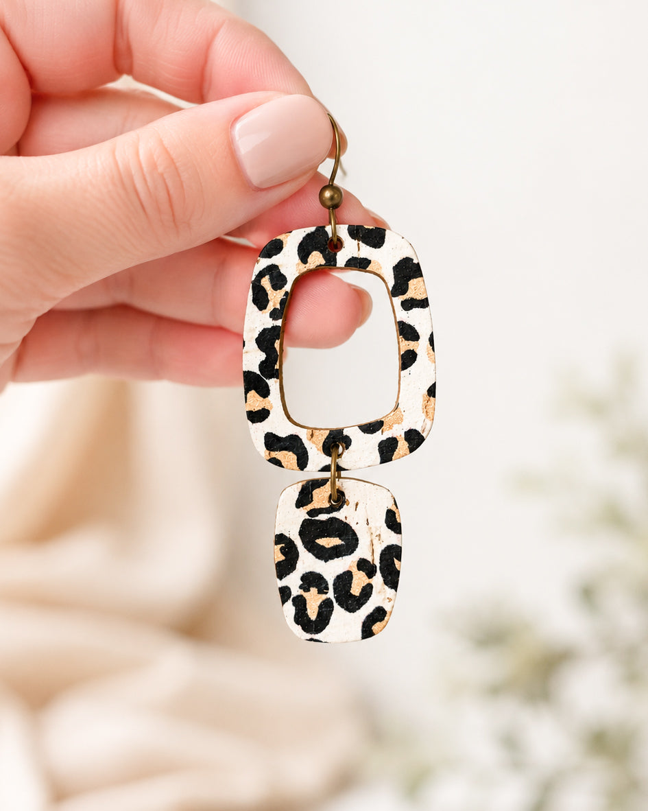 Hand holding a lightweight white leopard cork earring to show its size.