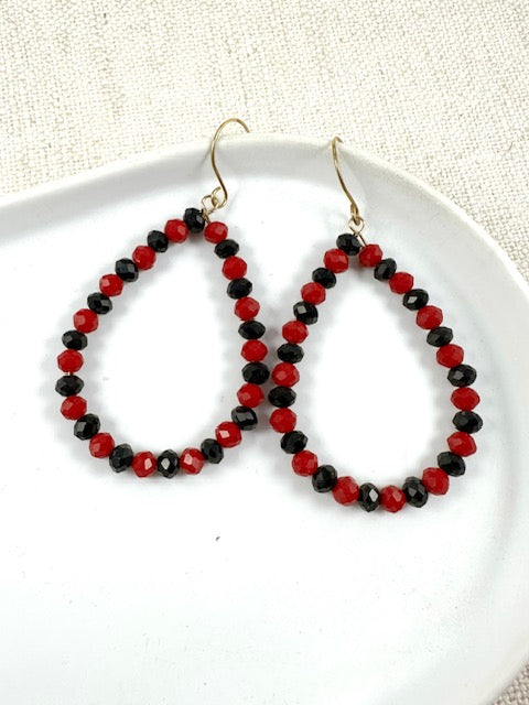 Beaded teardrop earrings with wine and black beads on gold hooks displayed on a white plate