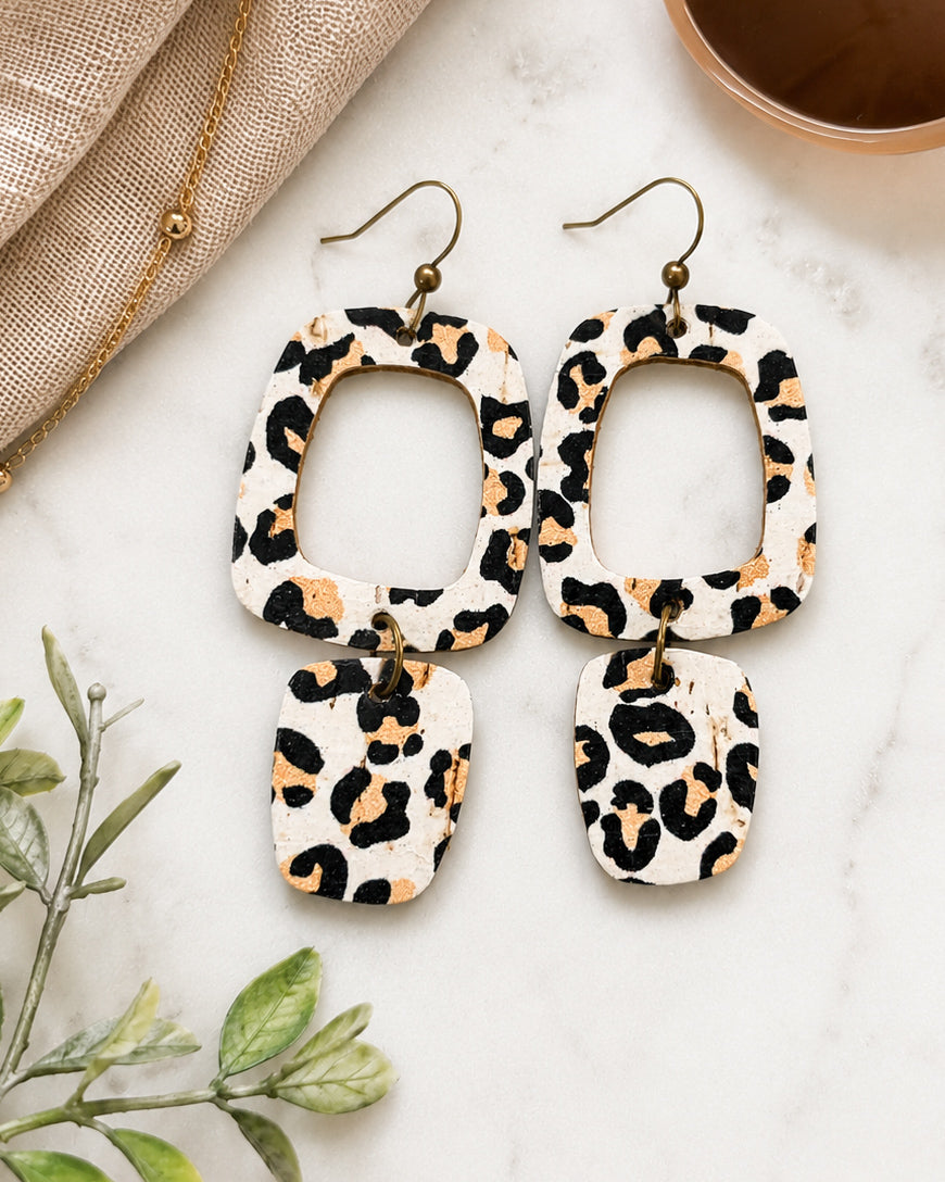 White leopard cork earrings styled on marble with coffee and neutral accessories.