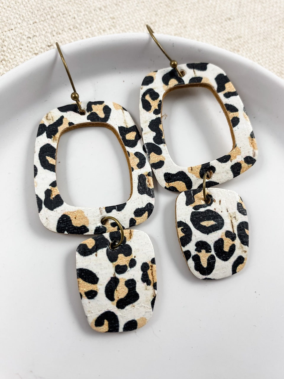 Handmade white leopard cork earrings resting in a white ceramic jewelry dish.