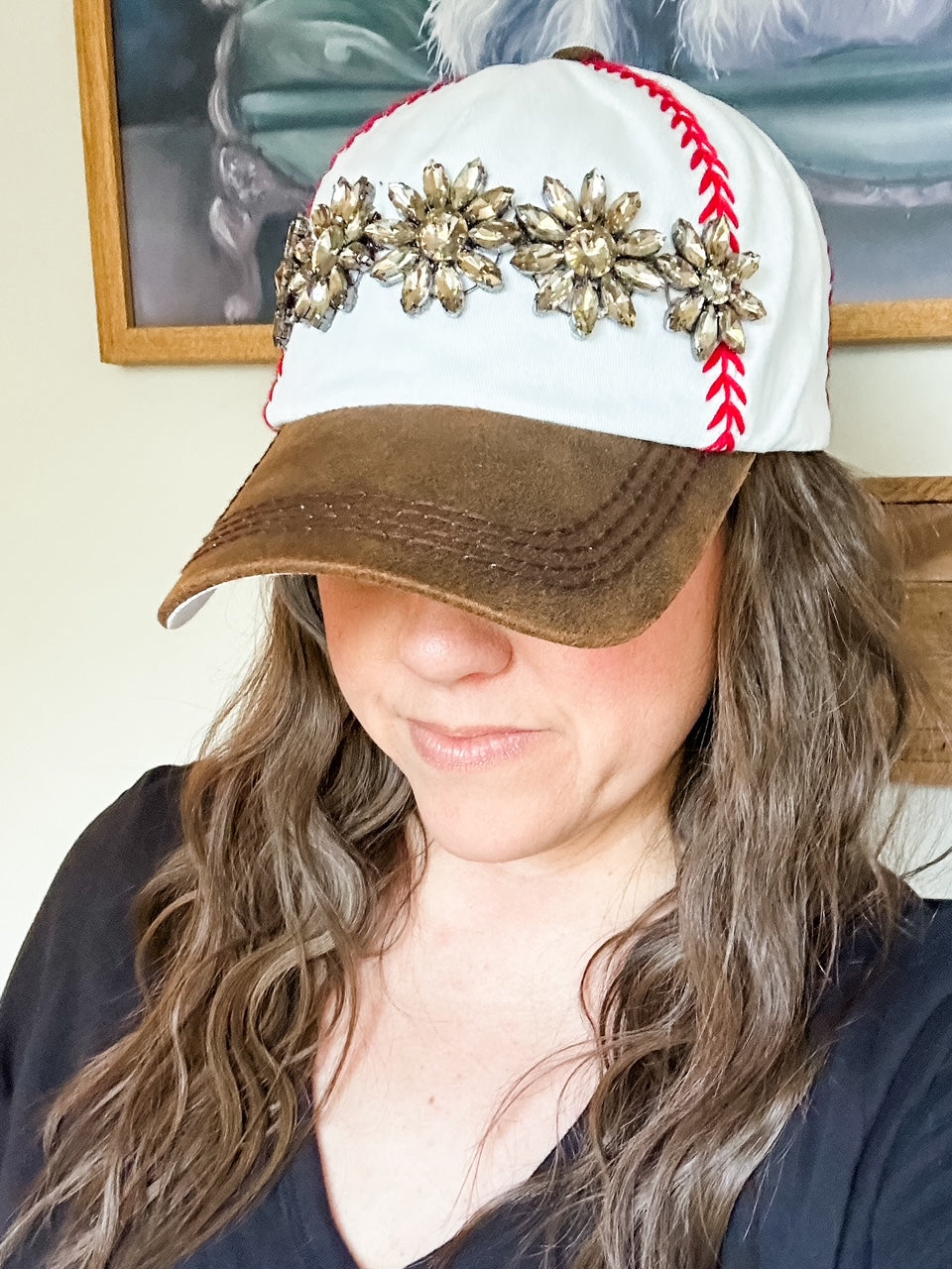 Woman wearing white baseball cap with red embroidered stitching, distressed brown bill, and topaz stone embellishment.