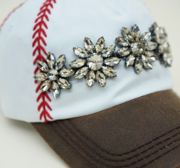 Close-up of white baseball cap showing red embroidered stitching, topaz stone embellishment, and distressed brown bill.