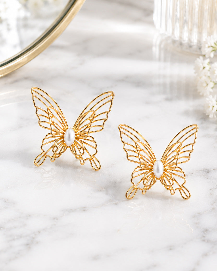 Gold filigree butterfly stud earrings styled on white marble beside a vanity mirror.