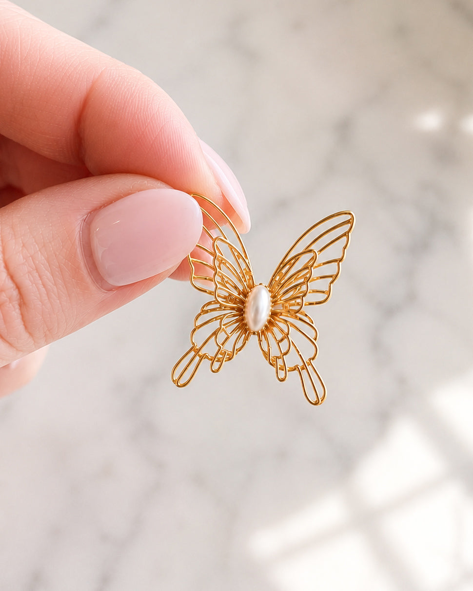 Hand holding a gold filigree butterfly stud earring with a faux pearl center to show its 1-inch size.