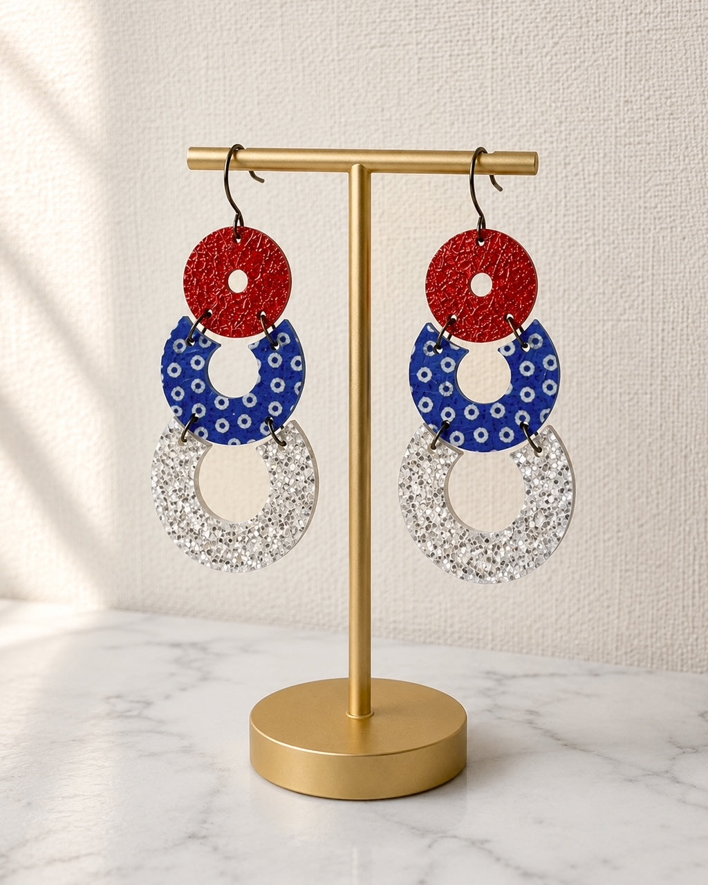 Firecracker Pop Earrings displayed on a gold stand featuring handmade cork and genuine leather patriotic details.
