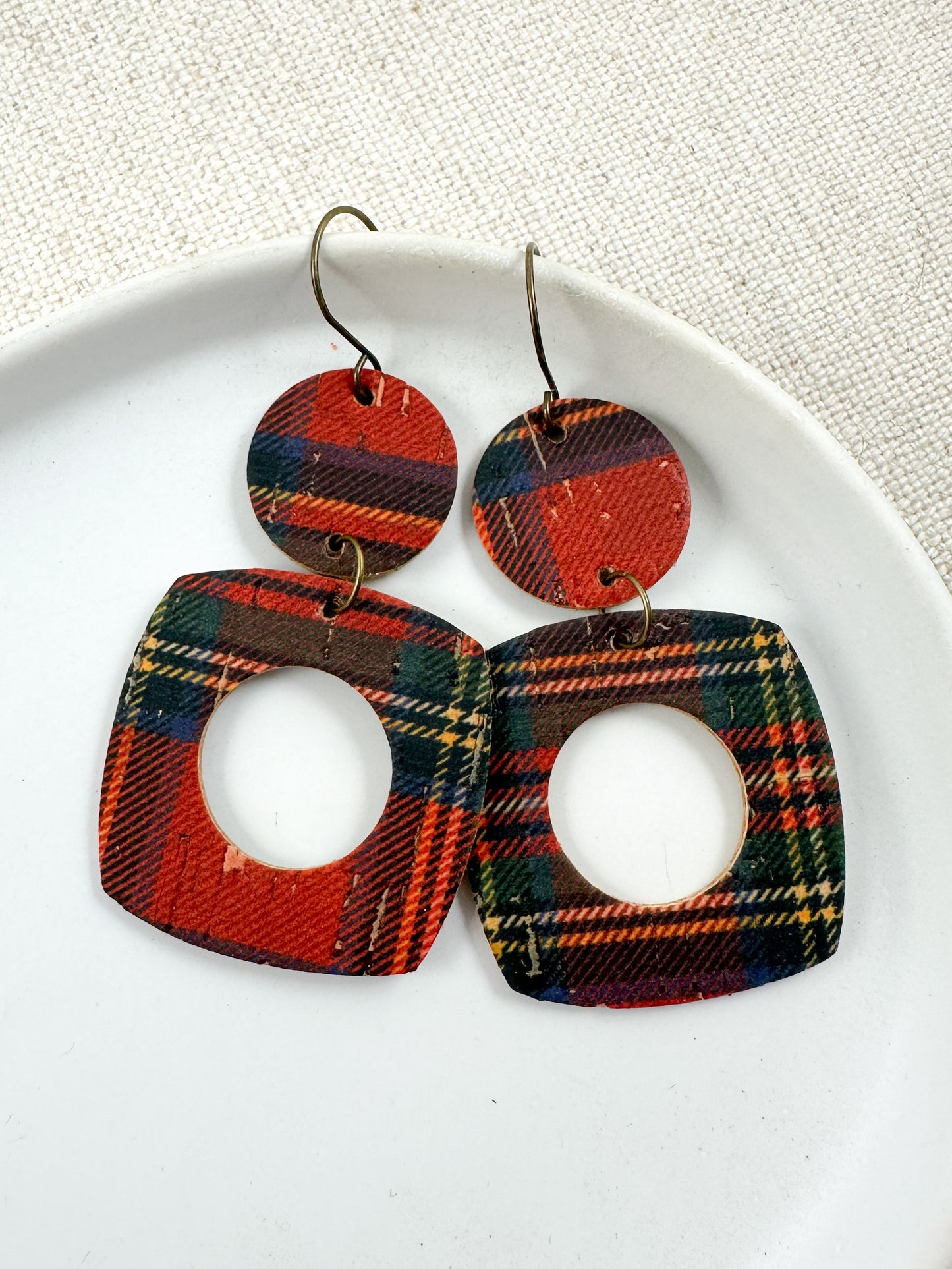 Geometric cutout earrings made from red and green Fireside Tartan Plaid cork displayed on a white dish.