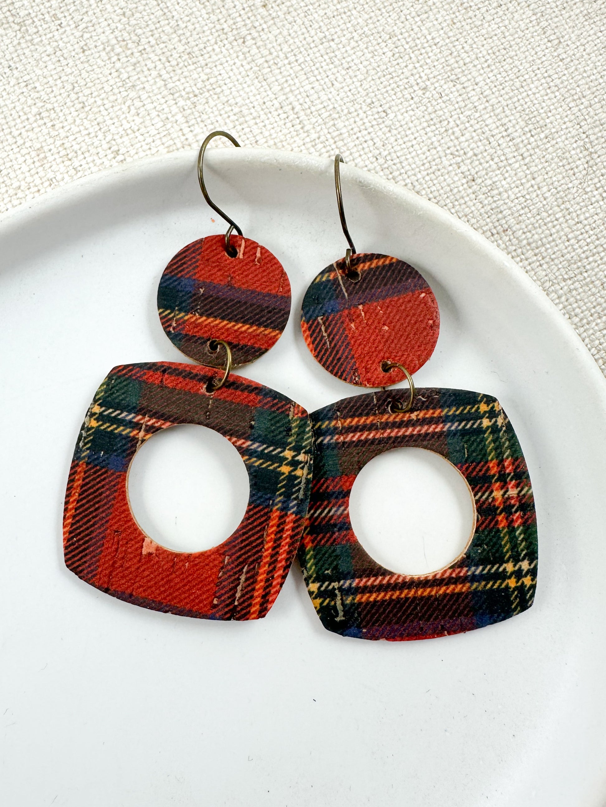 Geometric cutout earrings made from red and green Fireside Tartan Plaid cork displayed on a white dish.