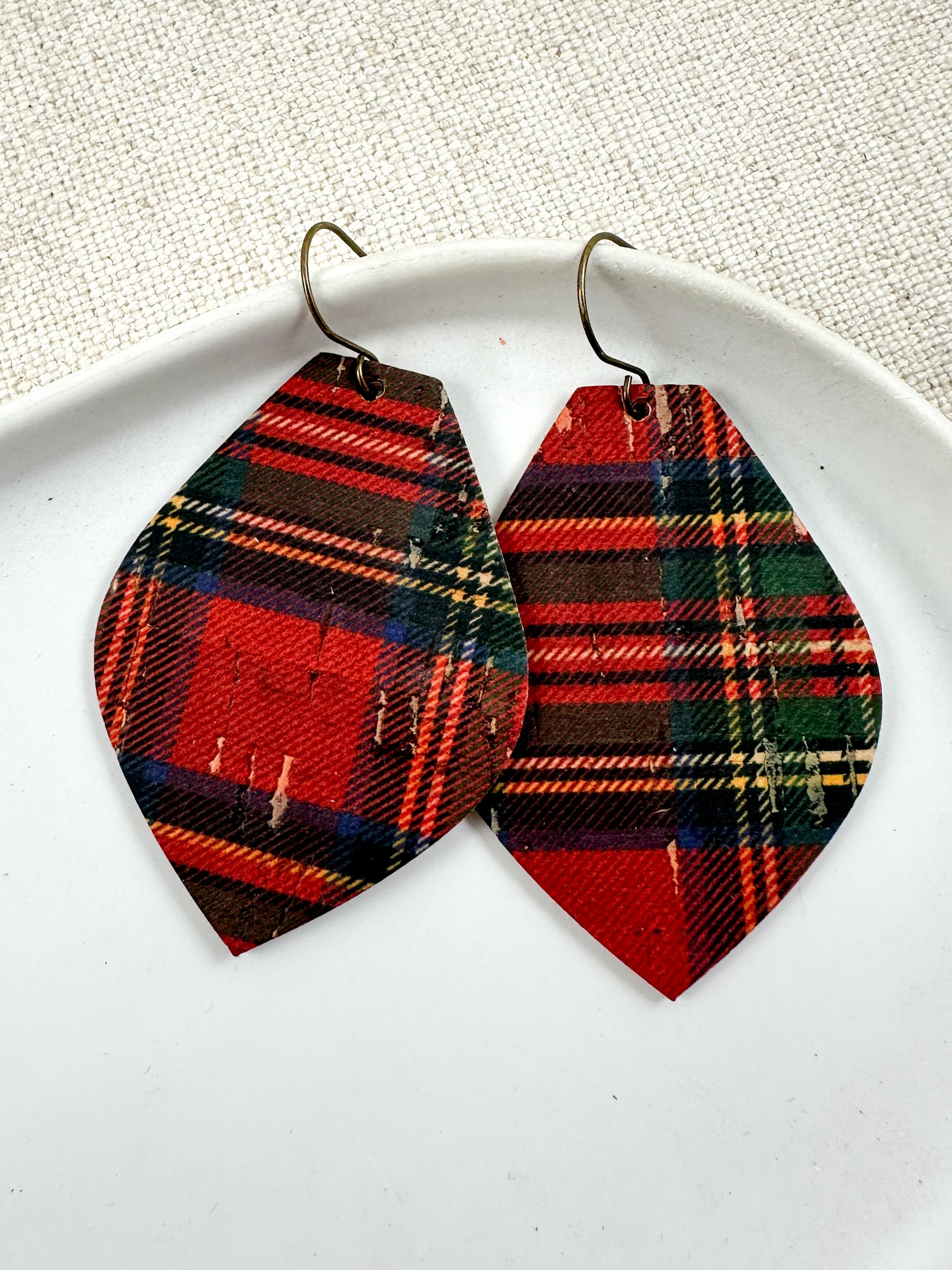 Red tartan plaid cork earrings displayed on a white dish.