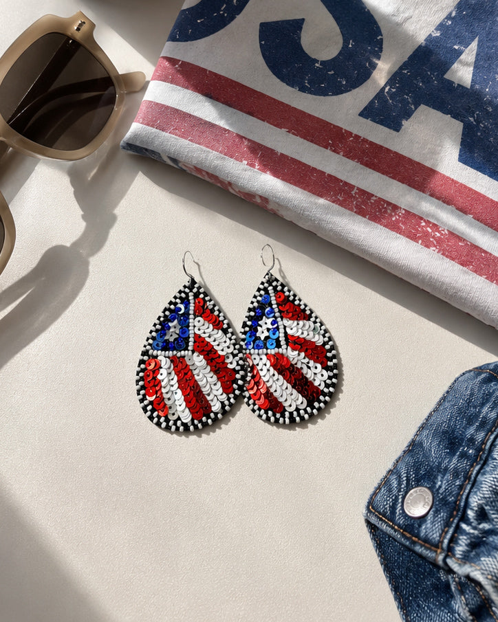 Patriotic American flag earrings styled with a patriotic graphic tee, denim jacket, and sunglasses for a Fourth of July outfit inspiration.