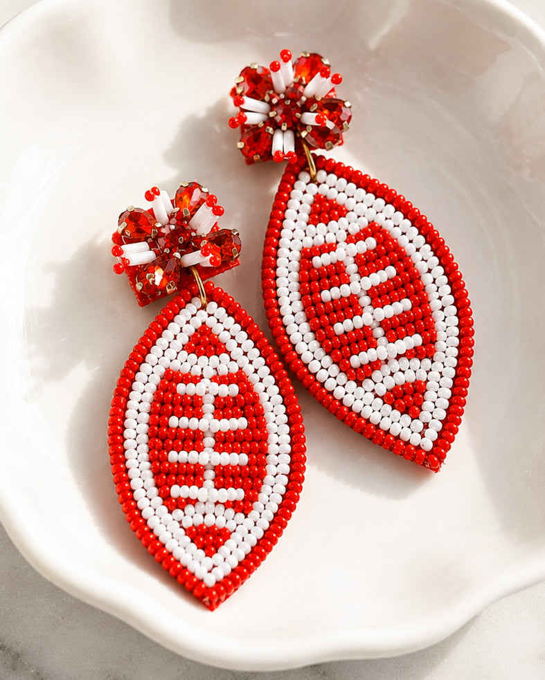 Football & Fireworks red beaded football earrings resting in a white ceramic jewelry dish