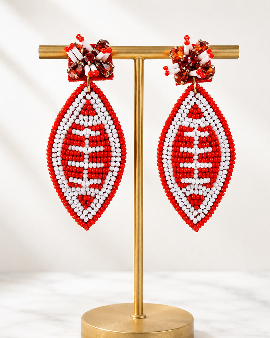 Football & Fireworks red beaded football earrings displayed on a matte gold jewelry stand