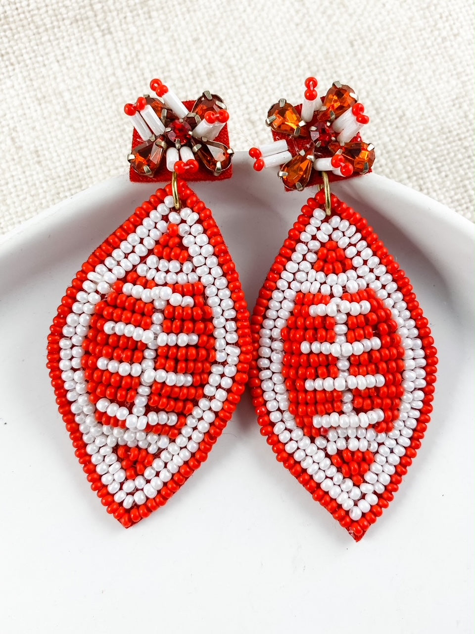 Football & Fireworks red beaded football earrings with crystal accents on a neutral linen background