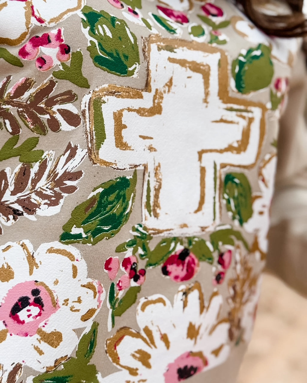 Close-up of floral cross design with pink flowers, green leaves, and metallic gold accents printed on a heather tan Christian graphic tee.