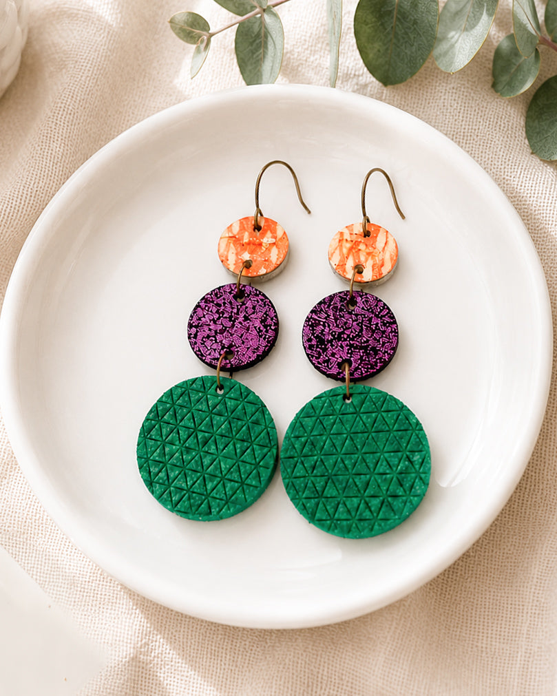 Handmade Garden Party leather and cork dangle earrings with coral, purple, and emerald green textured circles displayed on a white ceramic dish.
