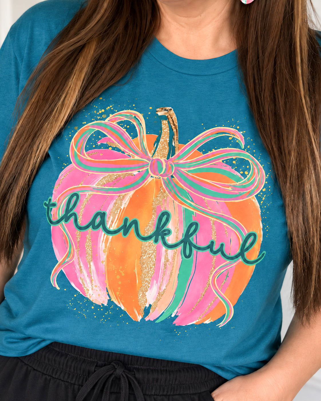 Close-up of woman wearing the Gilded & Thankful teal blue graphic tee with a colorful pumpkin and bow design.