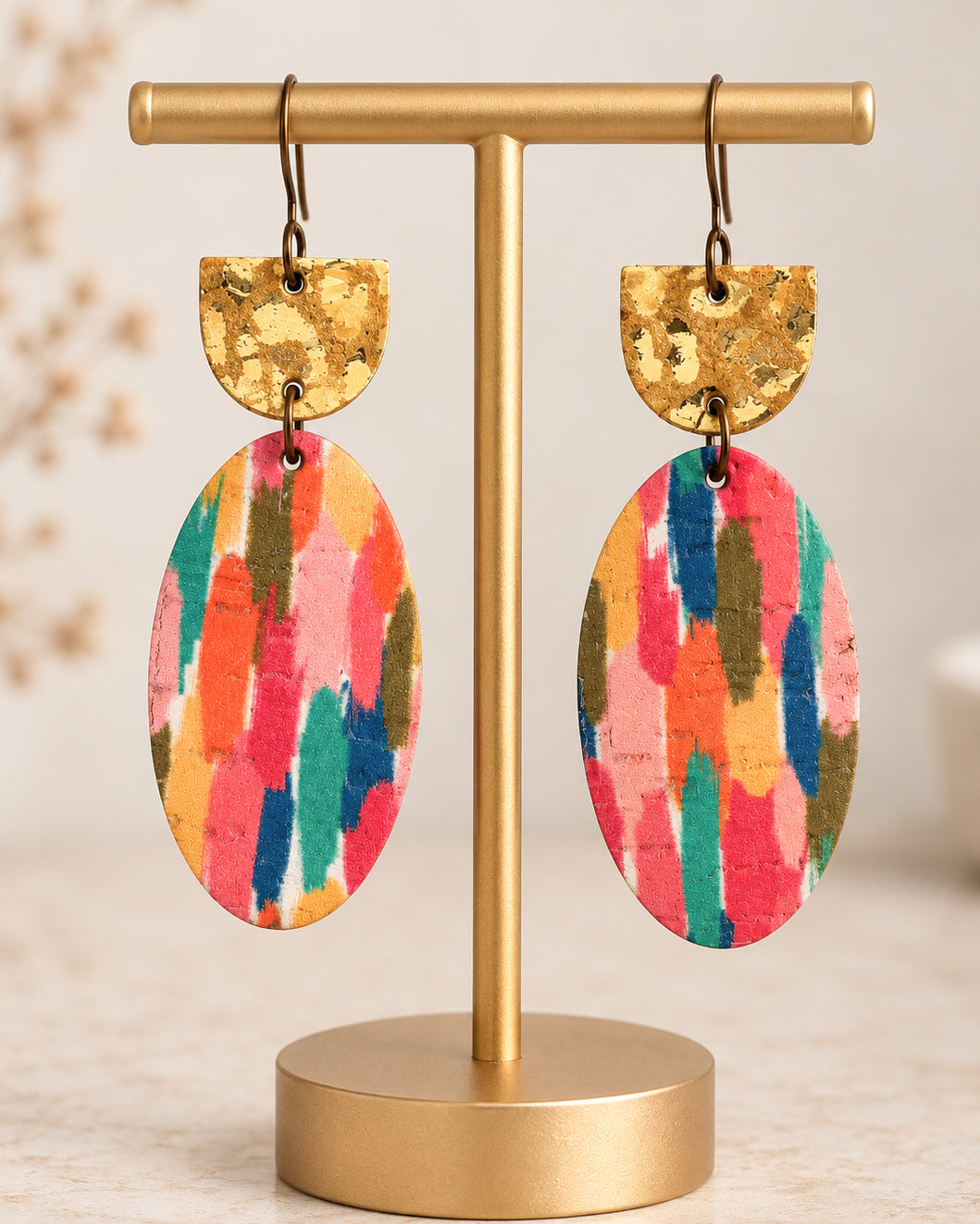 Colorful Gilded Brushstroke dangle earrings with metallic gold leather tops and oval leather drops displayed on a matte gold jewelry stand.